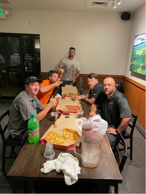 The image depicts a casual lunch setting with people enjoying comfort food while wearing branded t-shirts. This scene highlights the importance of team building and employee engagement in the HVAC industry, showcasing how NexTech fosters a positive work environment.