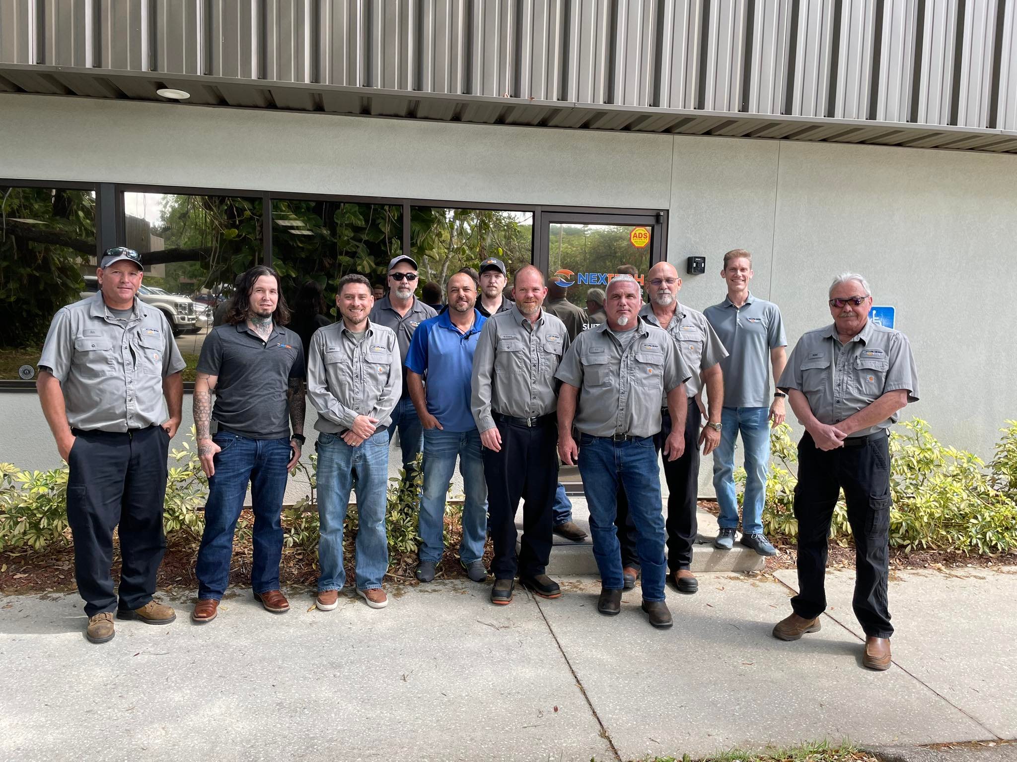 The image features a smiling team of professionals dressed in casual workwear, including jeans, standing together in a social setting. This reflects the collaborative spirit and approachable nature of NexTech, an HVAC company focused on building strong relationships with both its employees and clients.